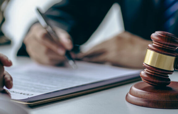 Two people at a desk signing a document next to a judge's gavel
