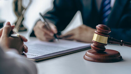 Two people at a desk signing a document next to a judge's gavel