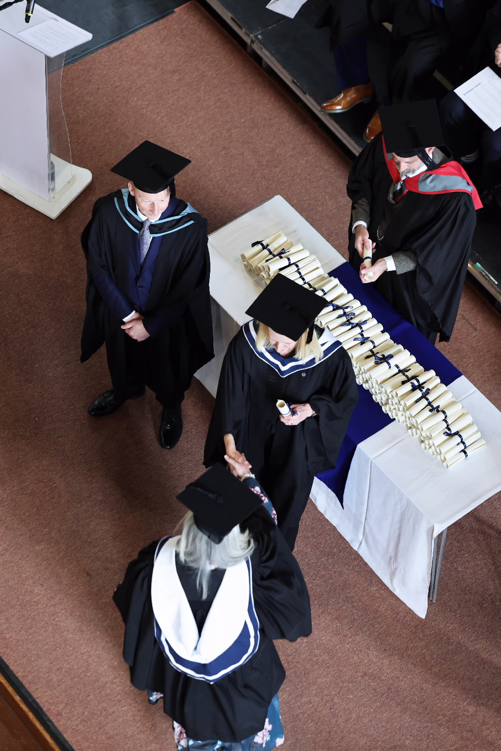 Overhead view of graduates receiving their rolled diplomas at a table.