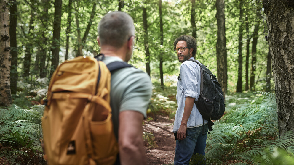 Two men wearing backpacks hiking in a forest