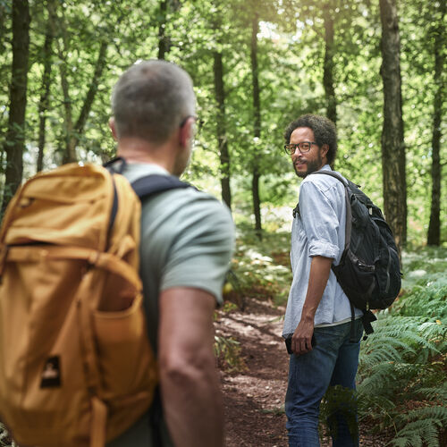 Two men wearing backpacks hiking in a forest