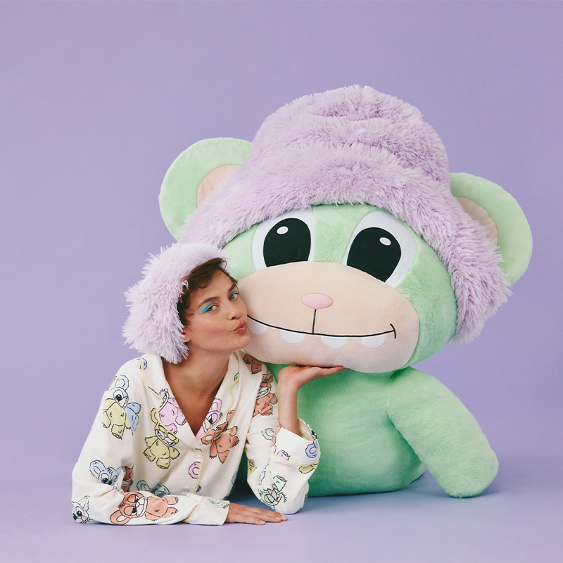 girl in printed pyjamas lying on the ground with a large plush scarebear