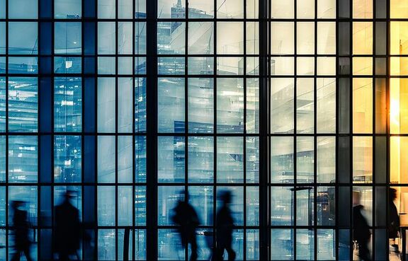 Silhouettes of people walking inside of glass office building