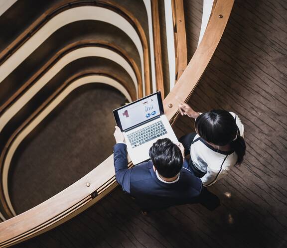 Man and woman looking at a laptop on the railing overlooking multiple stories of a building