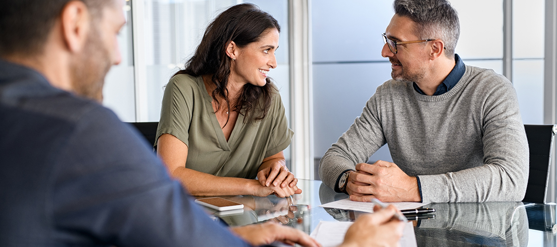 A couple in an office looking at each other sitting across from a man.