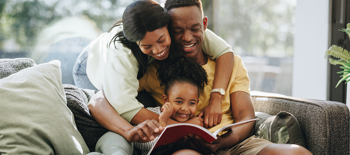 A mother and father embracing a child on a couch with a book.