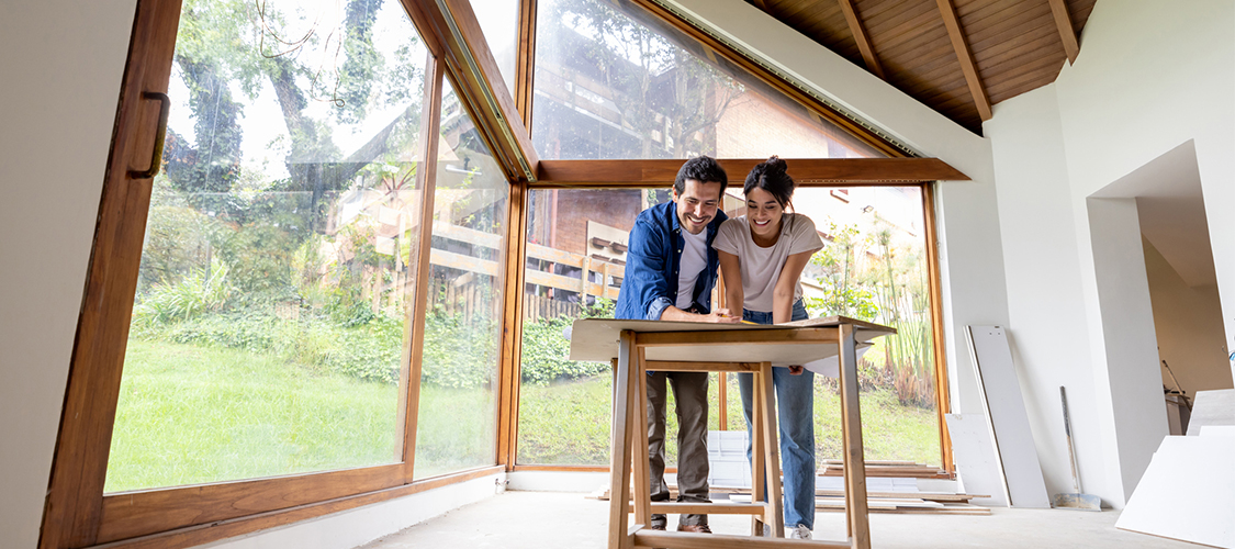 A couple looking at paperwork on a table in an empty room.