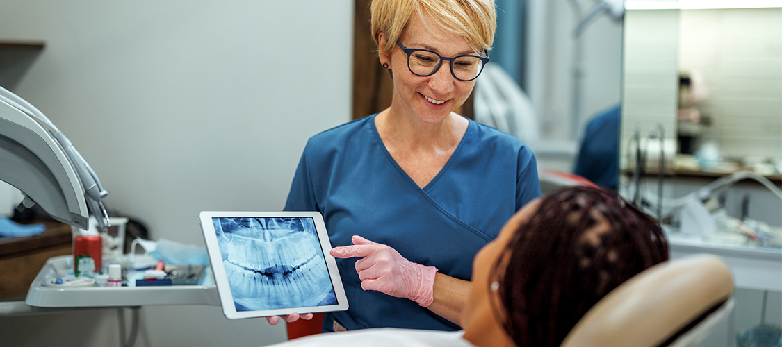 A woman showing an image on a tablet to a patient in a dental chair.