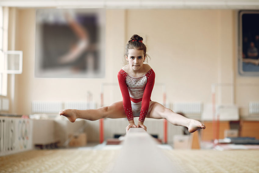 Mlada gimnastičarka izvaja vajo na bradlji.