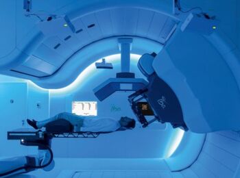 A PROTEUS ONE proton therapy unit supplied by IBA is shown hovering over a patient and preparing for a scan.