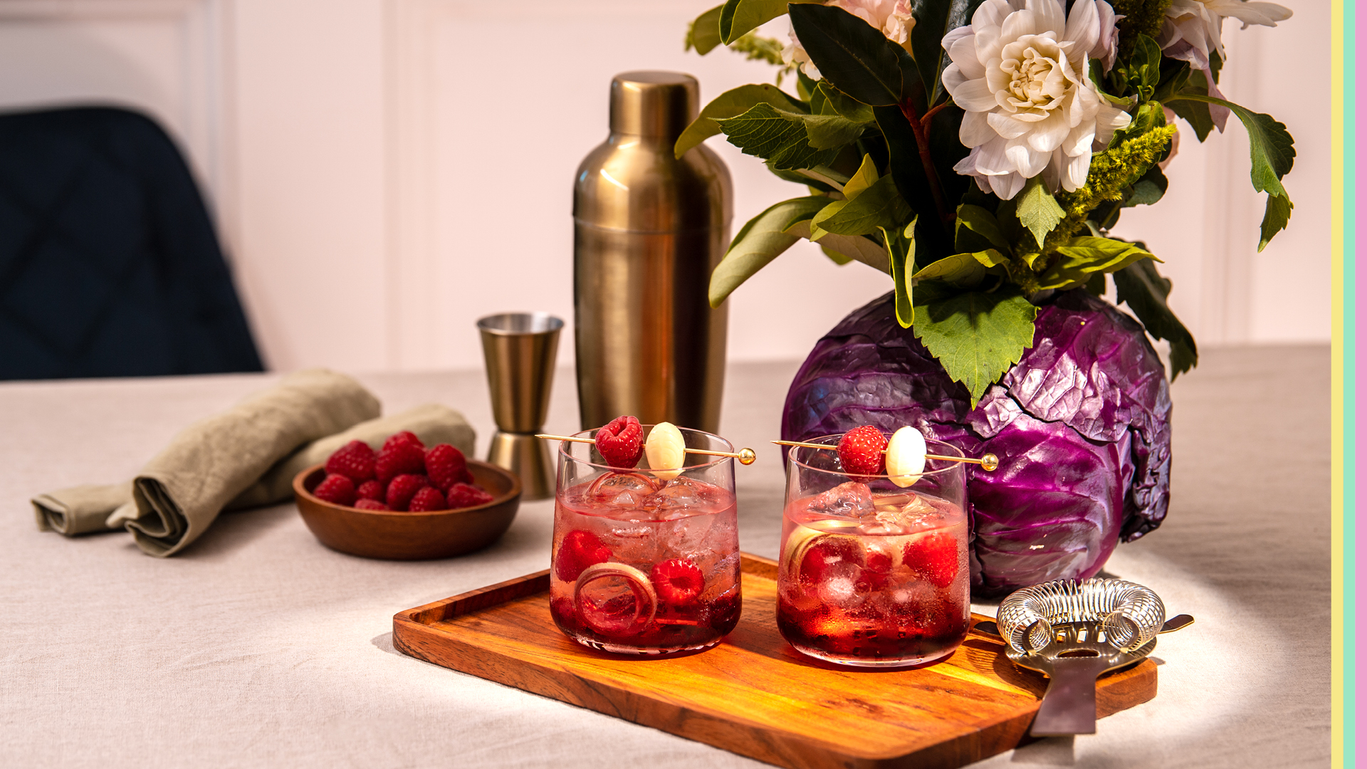 Two cocktail glasses with cocktail shaker raspberries and flowers in cabbage vase