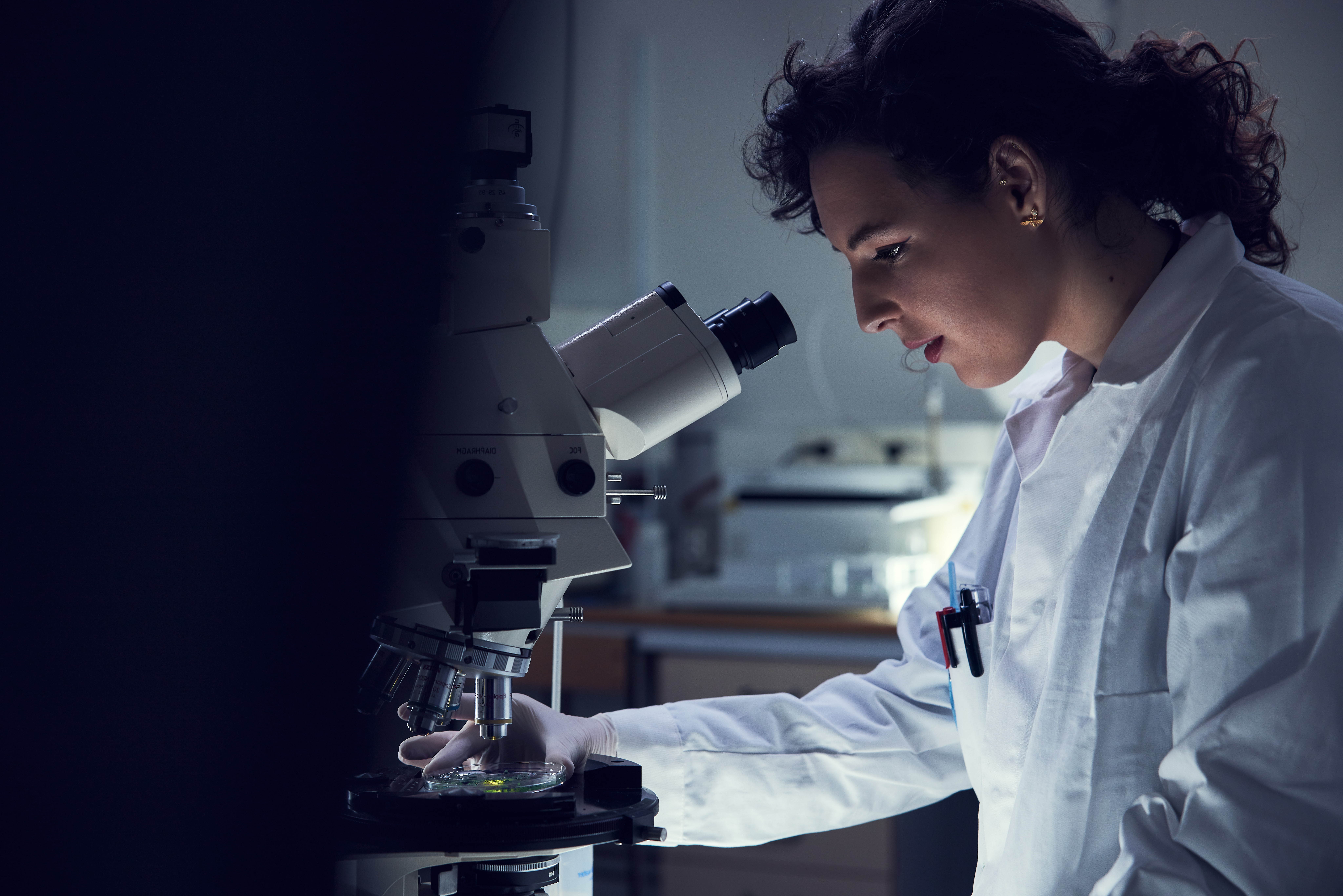 Woman in lab suit looking into a microscope