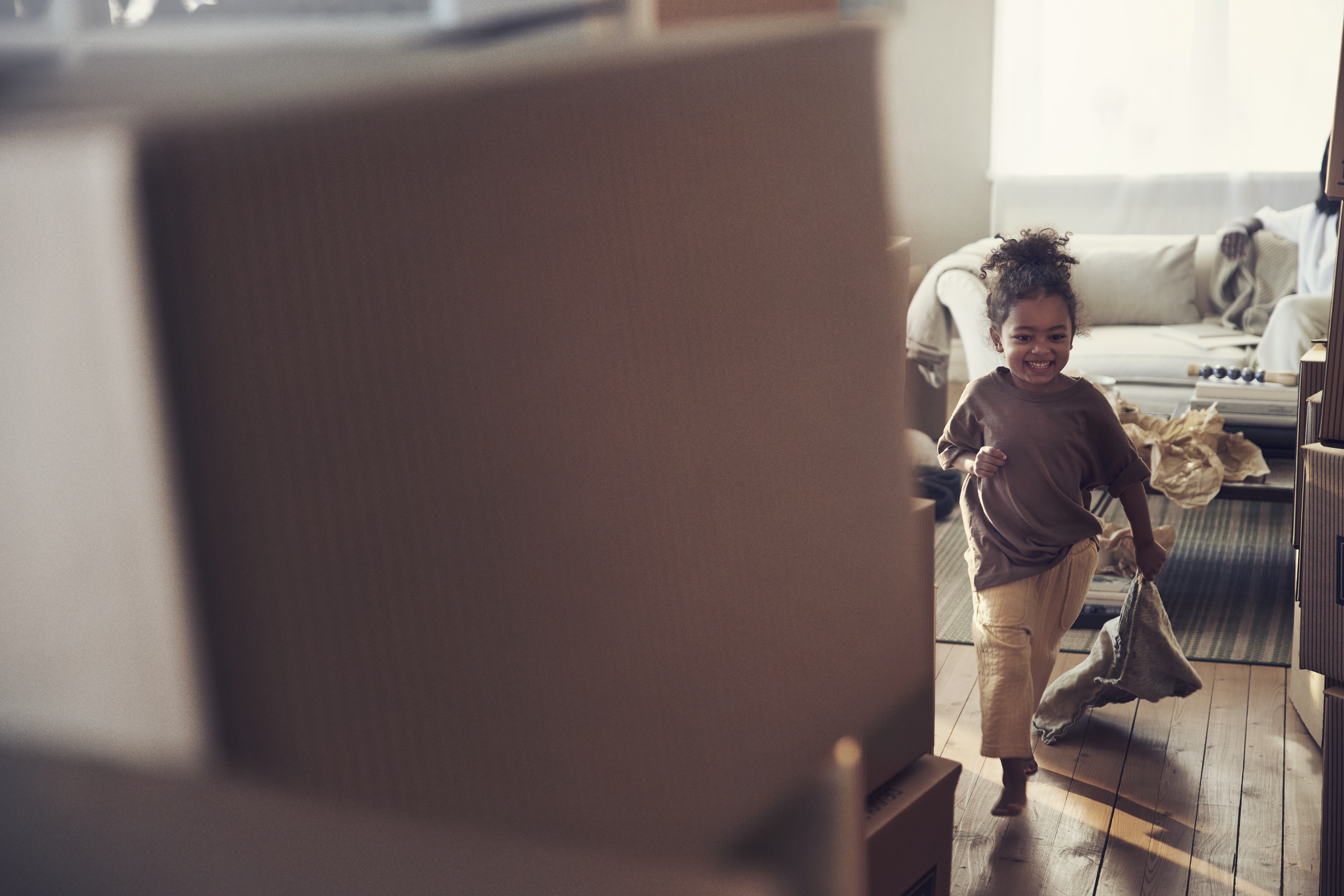 Litet barn springer leende i ett rum med flyttlådor.