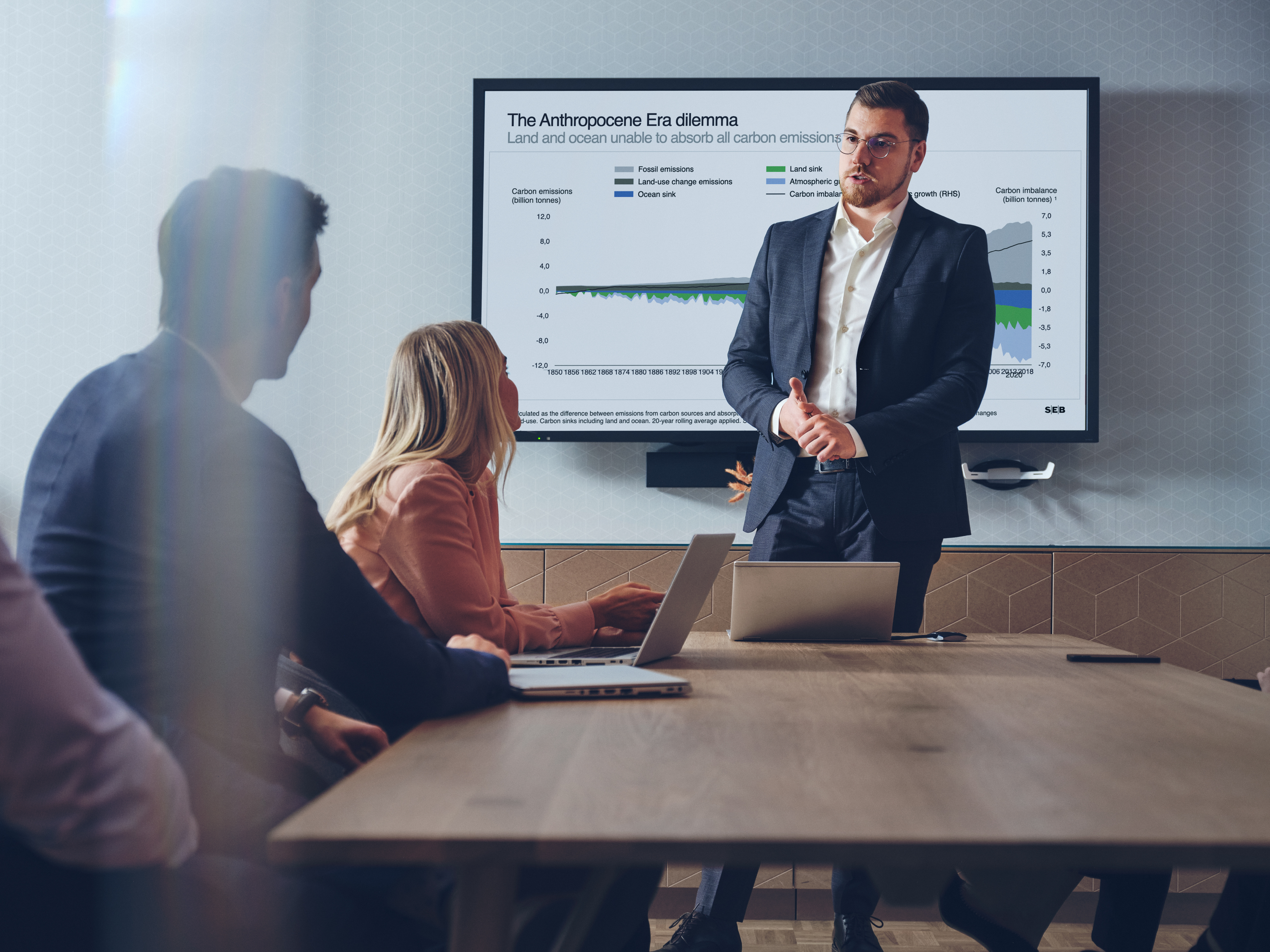 Three people discussing at a table and in front of a screen