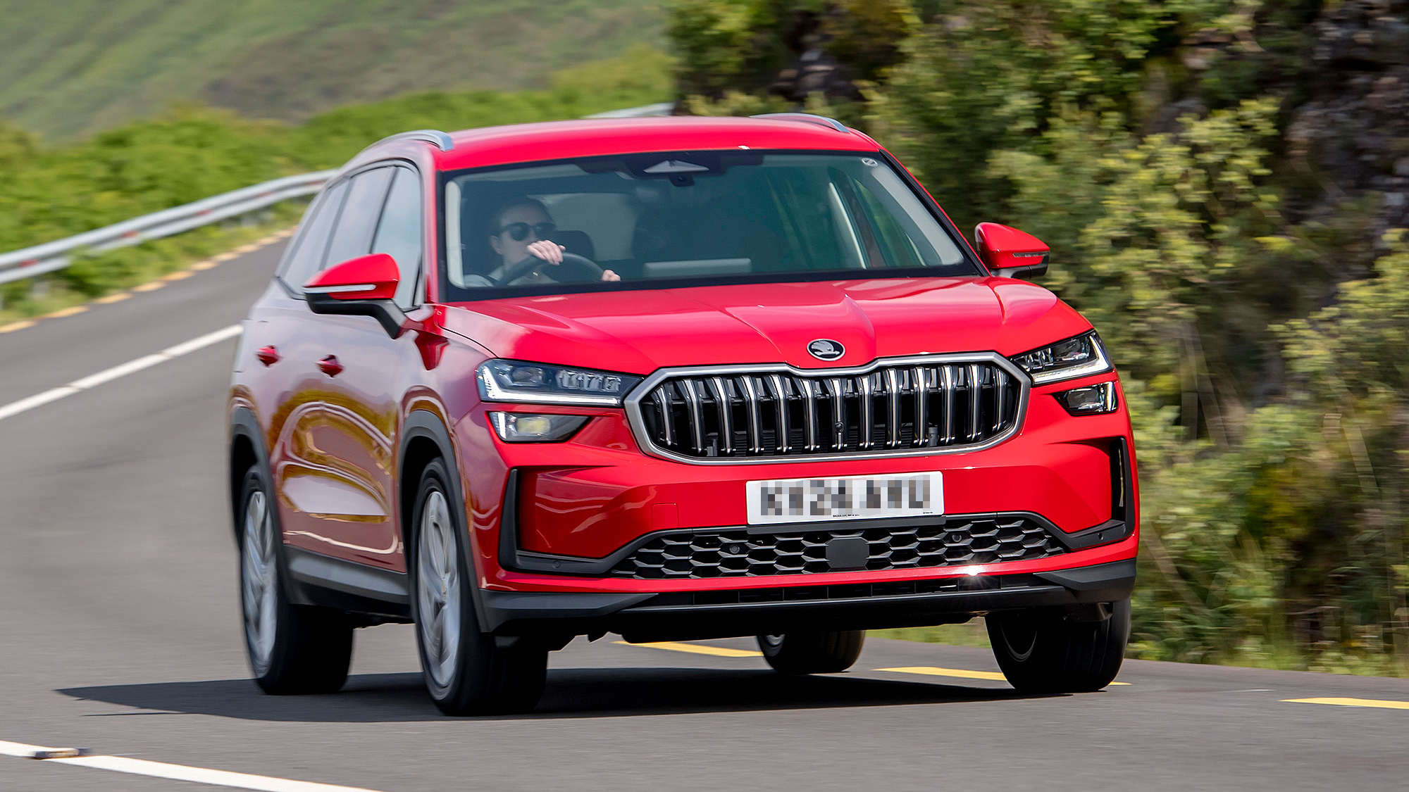 A bright red Škoda Kodiaq on a winding road, featuring a bold grille and black roof trim.