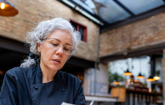 Female business owner looking over receipts at a table while using a tablet 