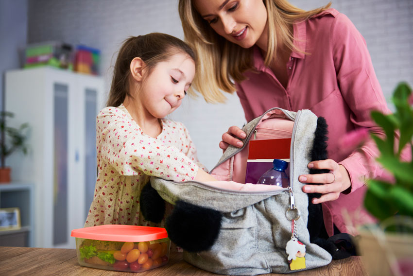 Mama hčerki pomaga v šolski nahrbtnik pospraviti šolske potrebščine.