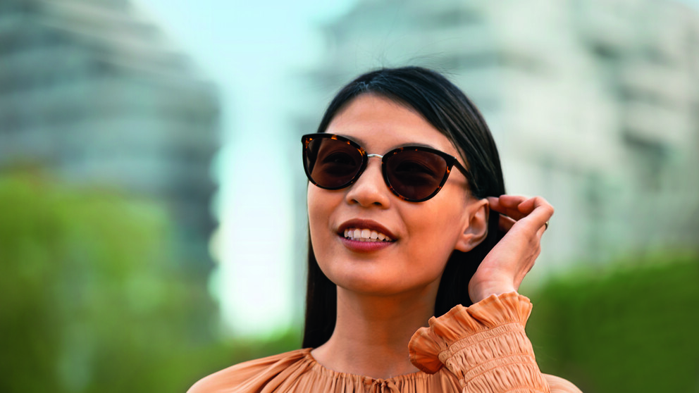 Lächelnde Dame mit Sonnenbrille und orangefarbenem Oberteil