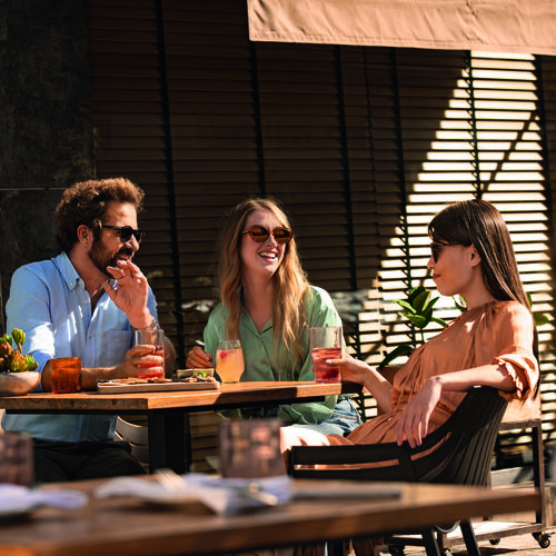 Three people wearing sunglasses while having lunch outdoors