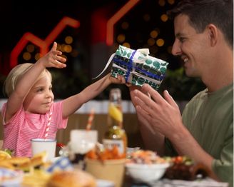 Dad receiving a wrapped Father’s Day gift from a child while sharing a meal together.