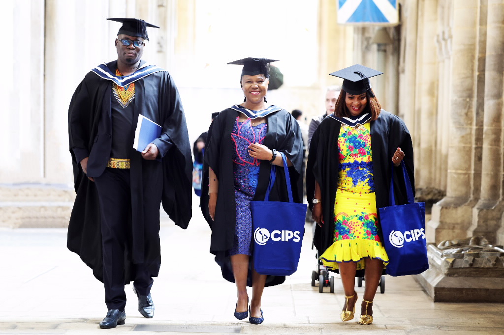 Three graduates in caps and gowns, wearing traditional African attire underneath
