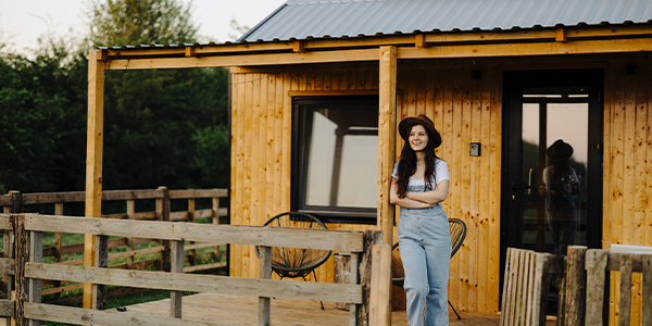 A woman outside of a tiny, wooden home.