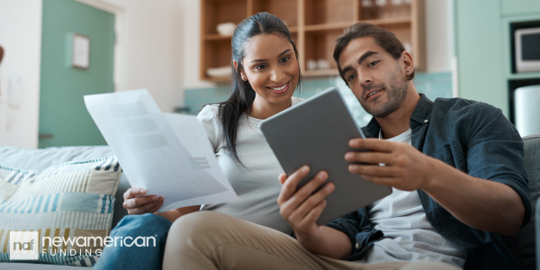 An Asian man and woman sit on a couch in their home going over paperwork 