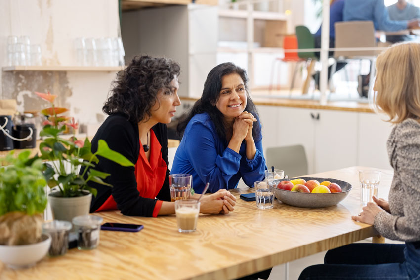 Tri ženske v pisarni trajnostno uživajo kavo iz klasičnih skodelic, skuhano v pisarniški kuhinji.