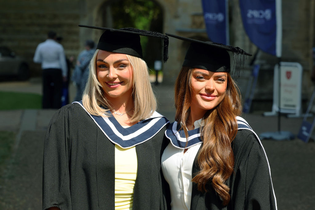 Two female graduates smiling outdoors in black gowns and mortarboards