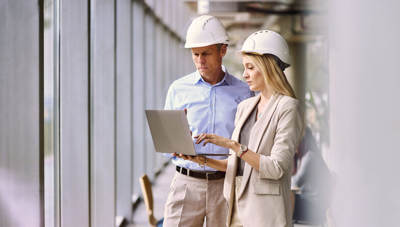 Two architects discussing with laptop in hard hats