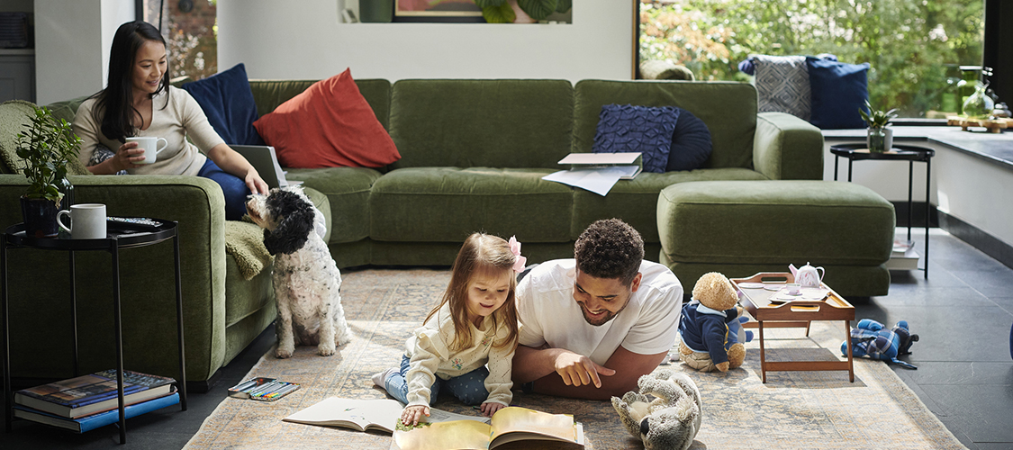 An Asian woman sits on a couch playing with a dog while a Black man plays on the floor with a little girl