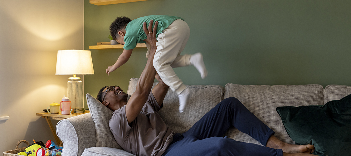 A Black man plays on the couch with his son