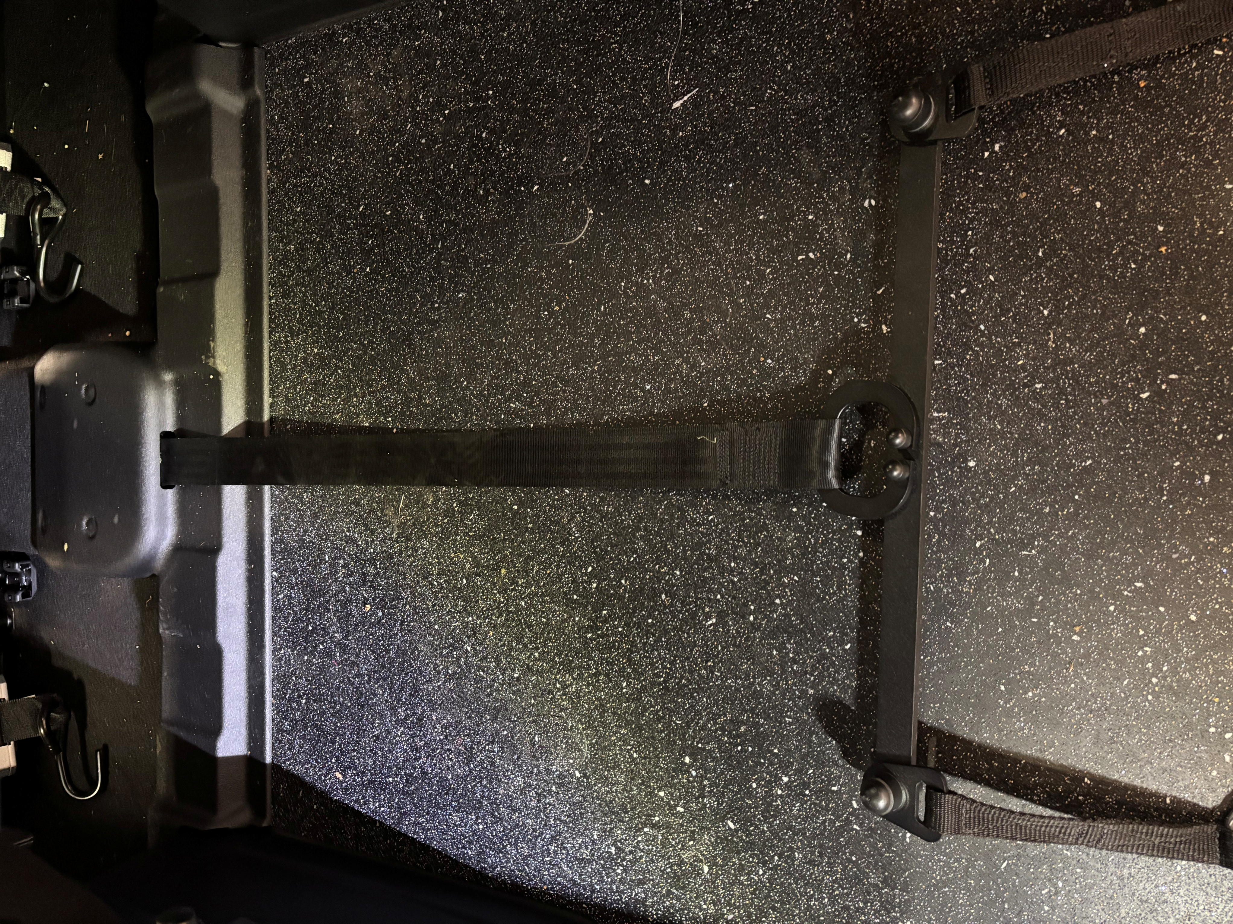 Close up view of the interior floor of a wheelchair accessible vehicle showing a black wheelchair restraint belt secured to floor mounted anchor points.