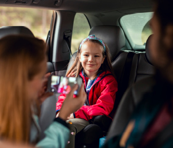Mati med vožnjo fotografira hčerko na zadnjih sedežih avtomobila.