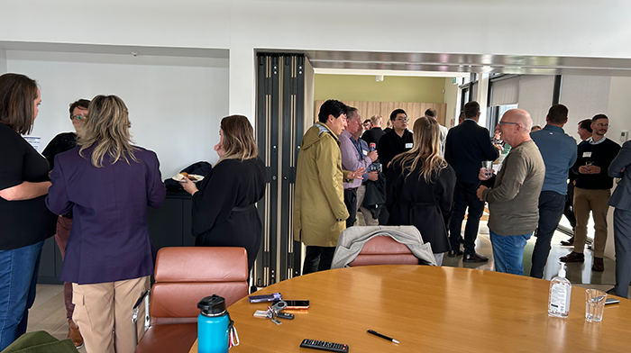 A busy indoor networking event showing a group of people standing and talking in an event space.
