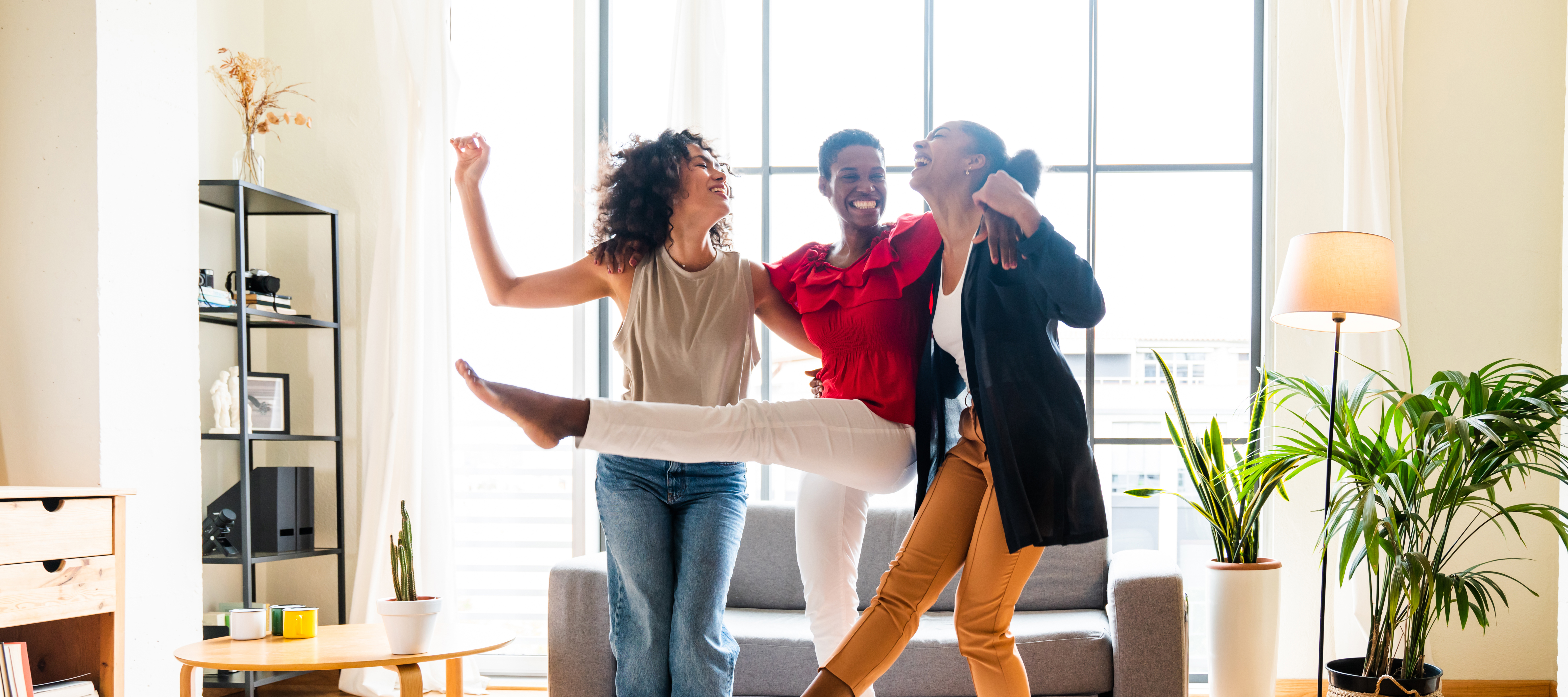 Three Black women dance together in celebration in a nice home