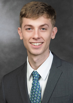 Headshot of Bradley Williams, who smiles while wearing a dark grey suit and a teal tie