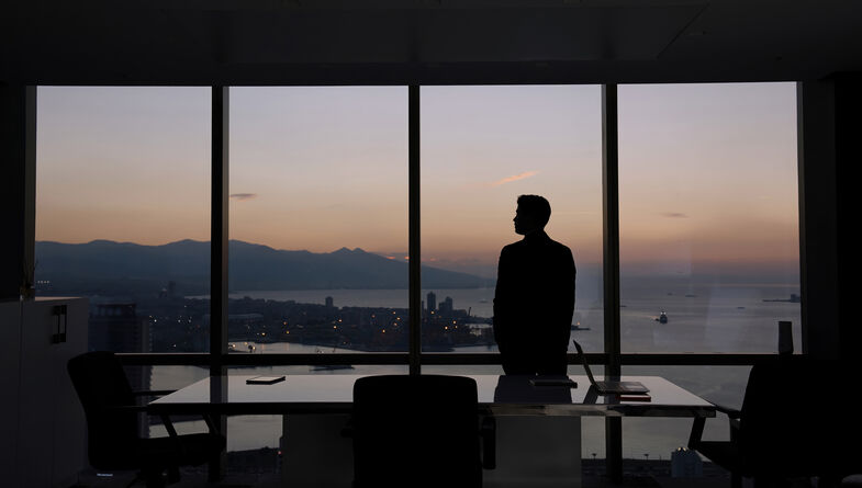 Businessman looking out office windows at sunset
