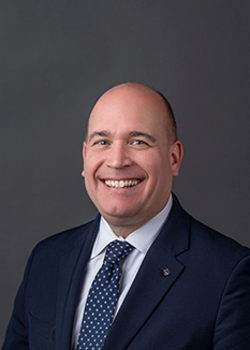 Headshot of David Nowak, who smiles while wearing a black suit and a blue tie