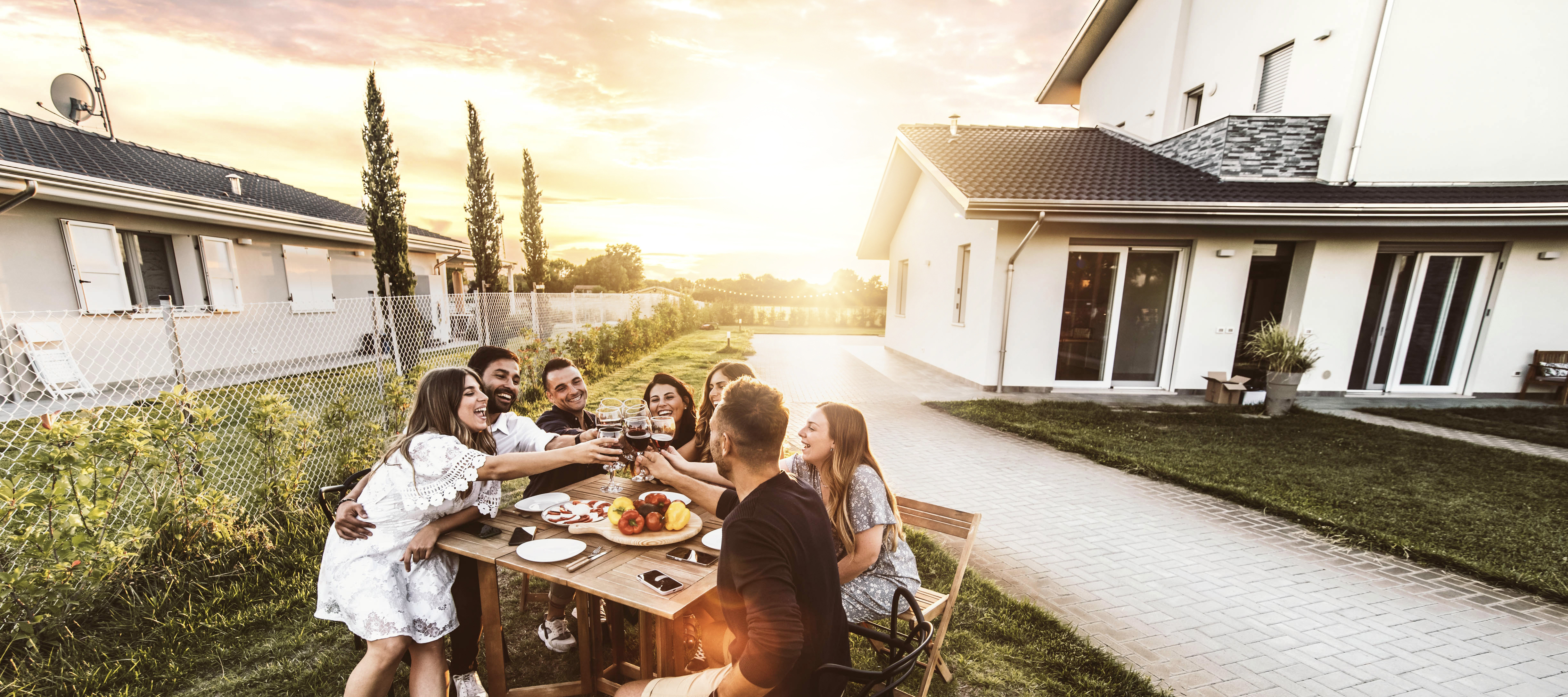 A group of friends happily share a meal outside of a nice home