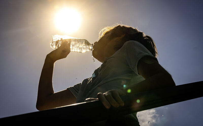 woman drinks bottle of water outside in the hot sun