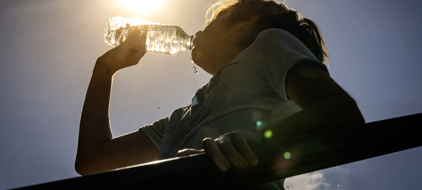 woman drinks bottle of water outside in the hot sun