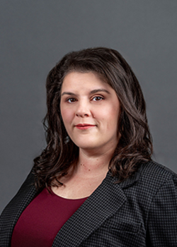 Headshot of Emily Saska, who smiles while wearing a maroon blouse and black blazer