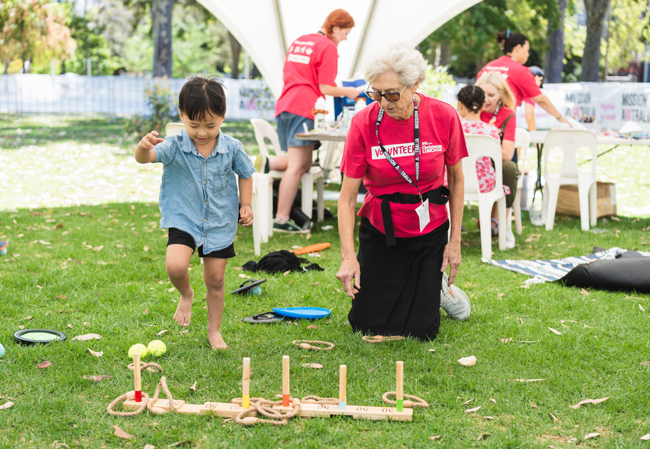 A young lady plays ring toss with an elderly Christmas Lunch in the Park volunteer.