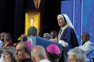 Mother Agnes Mary stands at the podium looking at the Convention attendees
