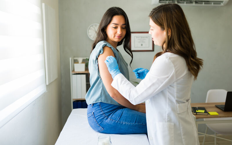 health care worker administers flu shot to woman in a clinic exam room