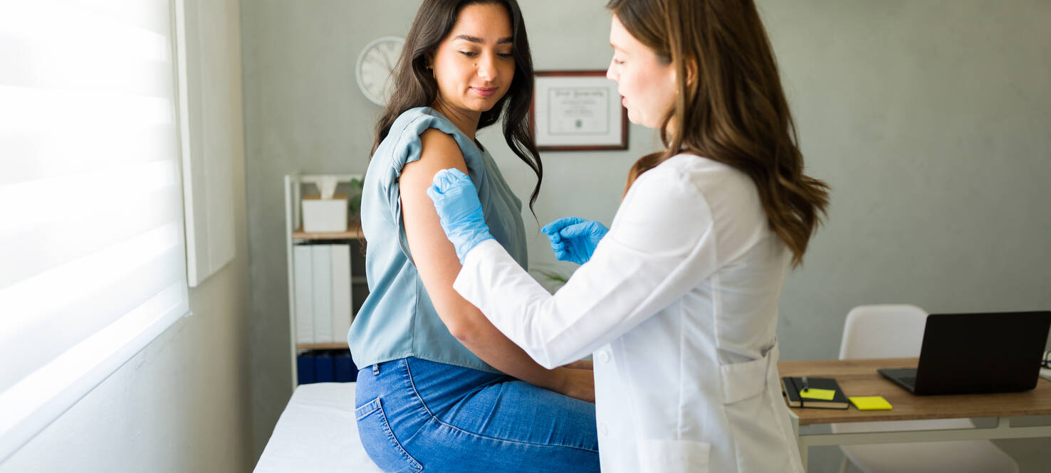 health care worker administers flu shot to woman in a clinic exam room