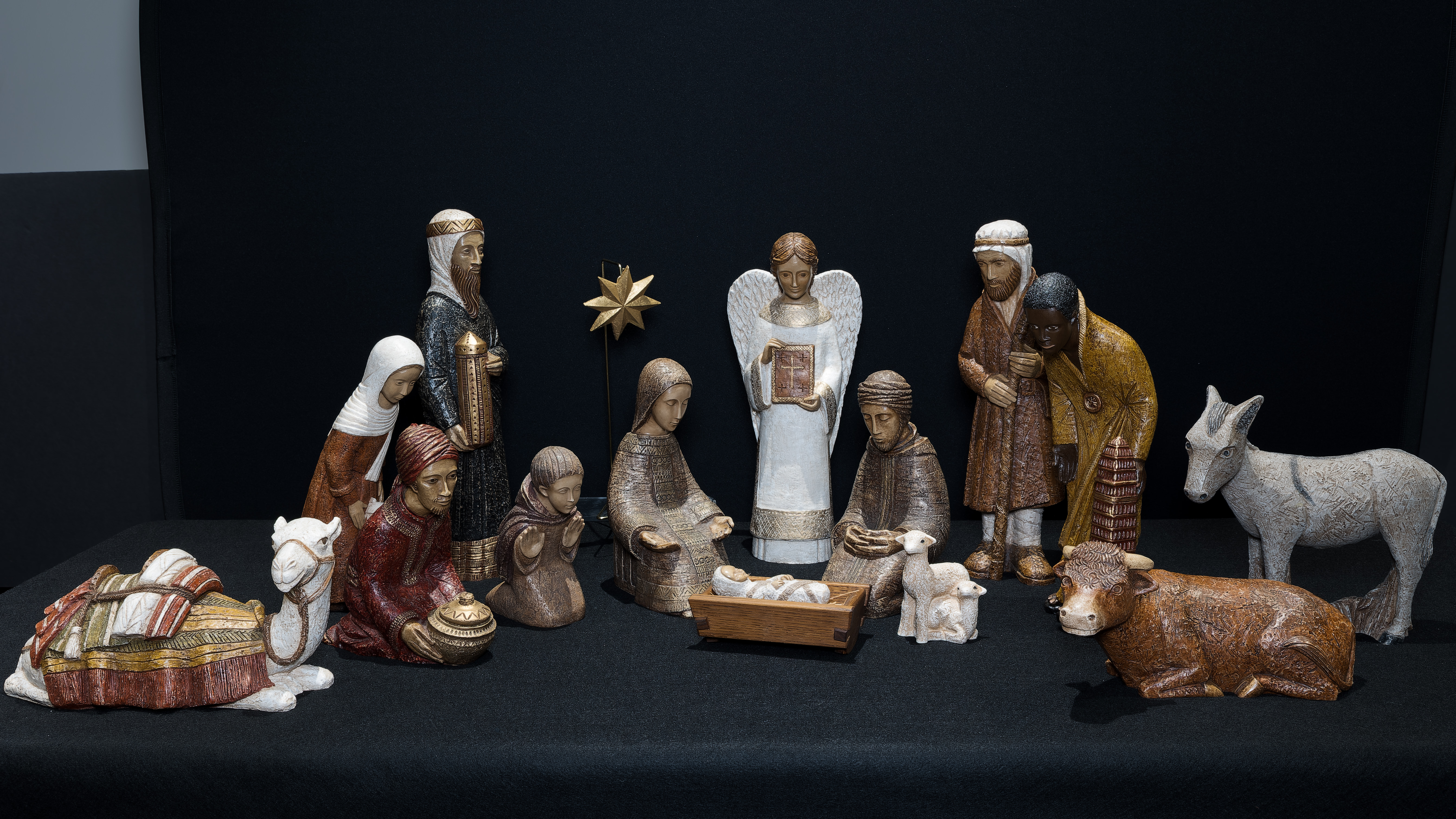 Image of a painted stone Nativity featuring the Star of Bethlehem, an Angel, the Holy Family, the 3 Magi, 3 shepherds, a donkey, cow, sheep, & camel.