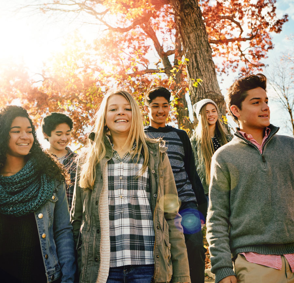 A group of teenagers walk down outdoor steps surrounded by autumn trees with sunlight shining through the leaves.
