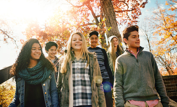 A group of teenagers walk down outdoor steps surrounded by autumn trees with sunlight shining through the leaves.